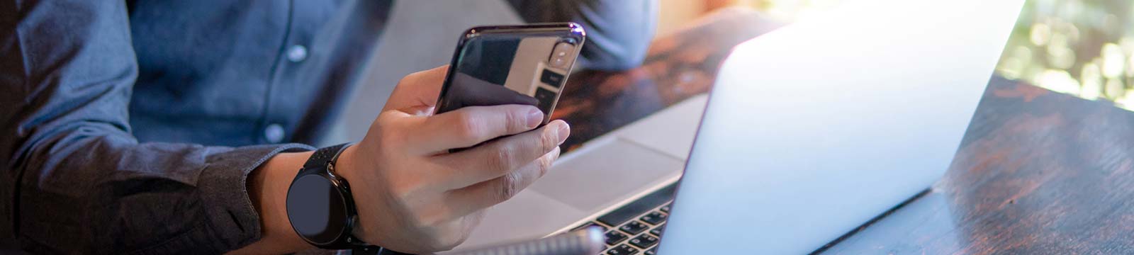 Man holding phone in front of laptop.