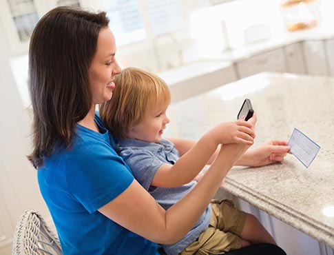 Mom and son taking photo of check at home in kitchen.