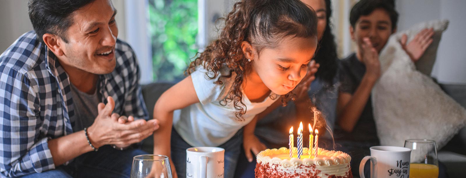 Girl blowing out birthday candles at home with family.