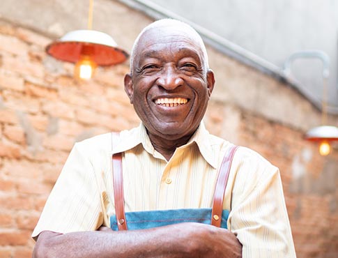 Smiling man wearing apron in front of brick wall.